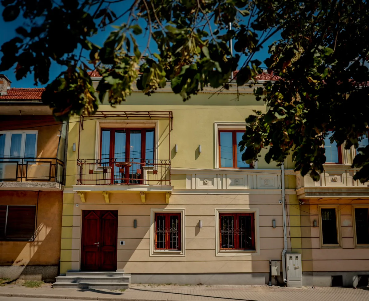 PAPARAZZI-Fassade und Balkone unter belaubten Zweigen